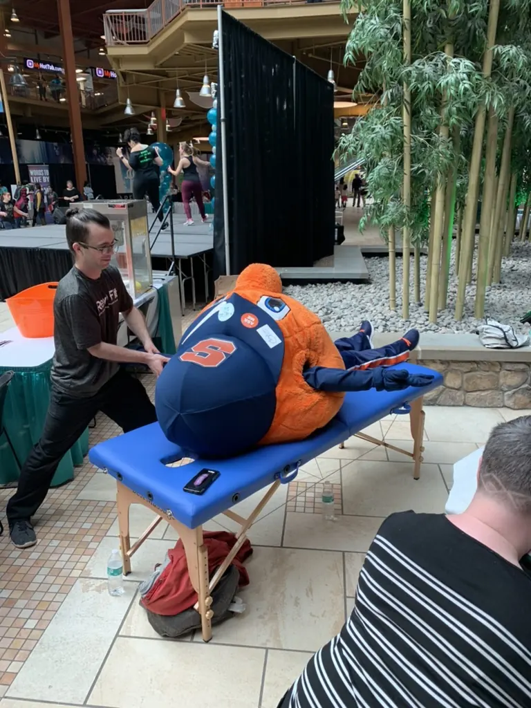 Otto the Orange, the Syracuse University mascot, on a Hand in Health massage table