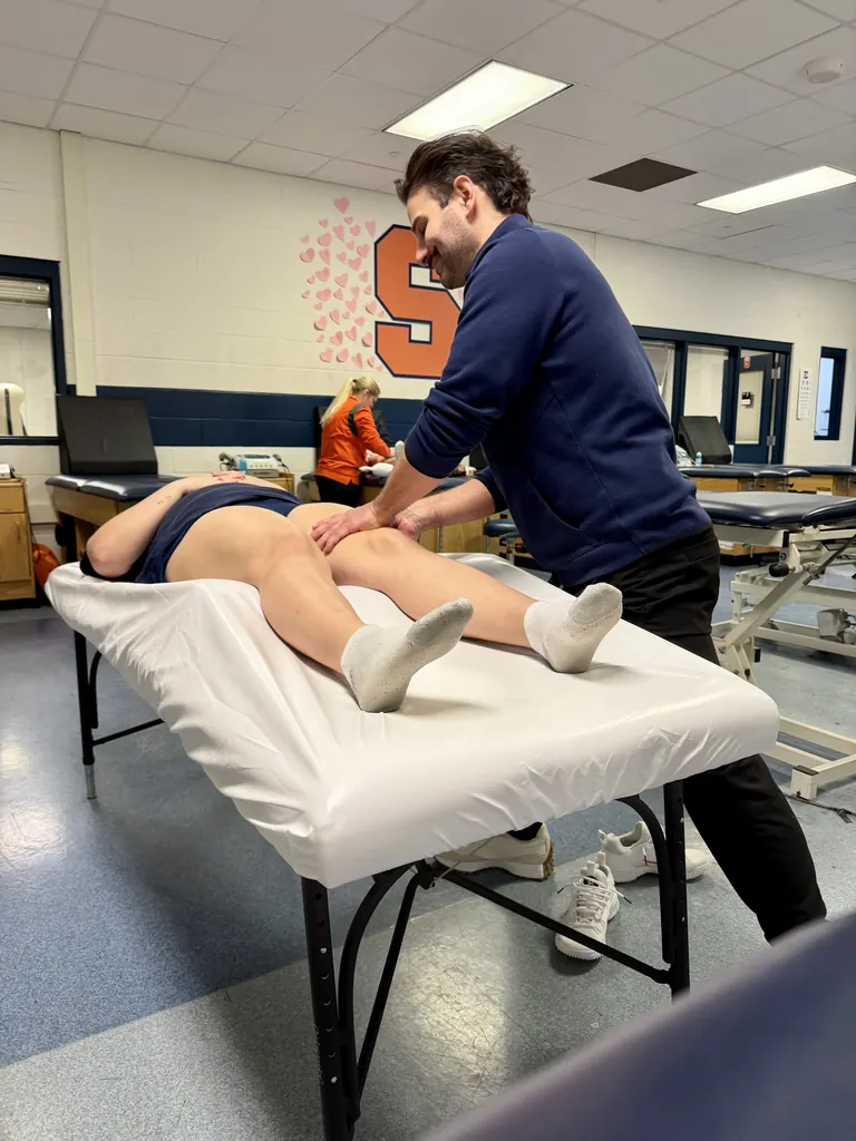 Hand in Health massage therapist working on an athlete's hamstring at Syracuse University